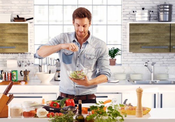 Handsome man cooking at home preparing salad in kitchen.