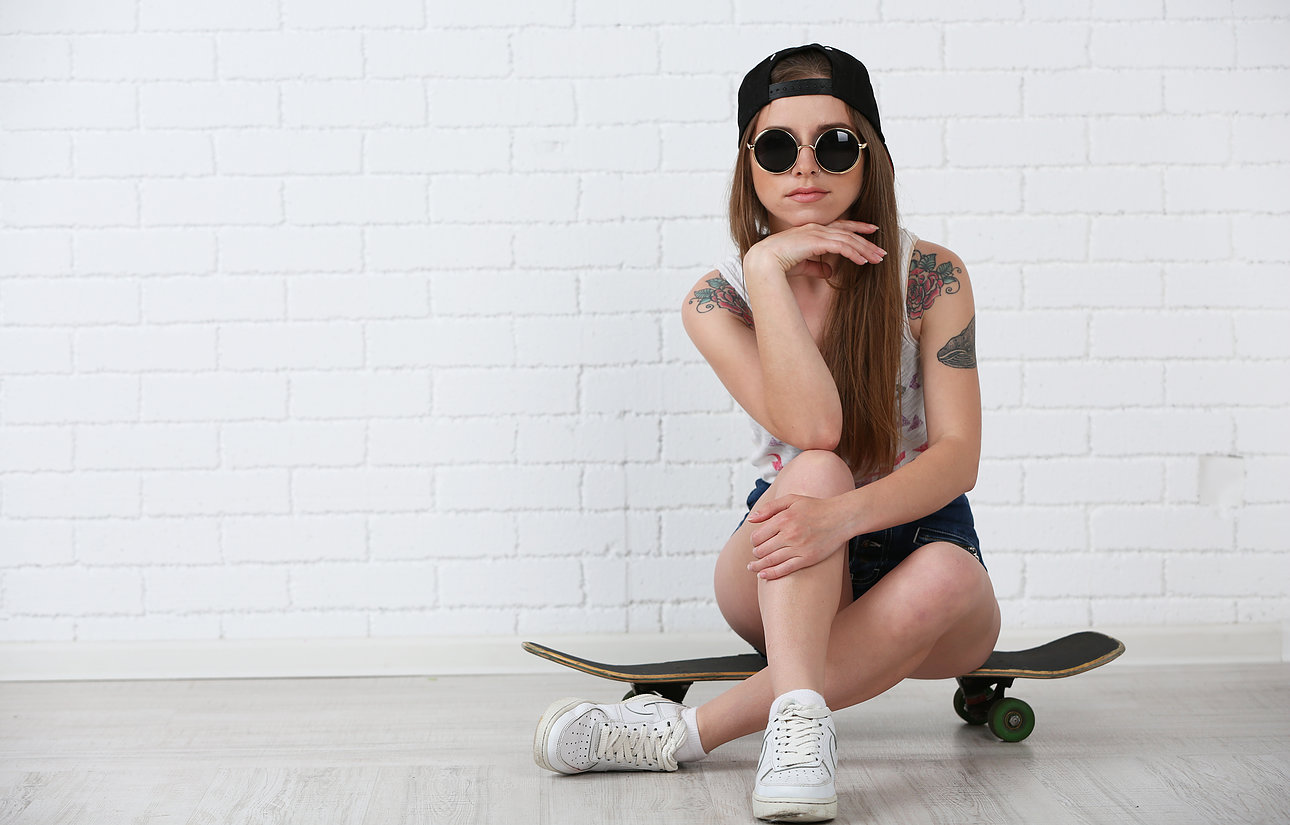 Beautiful hipster girl with skateboard on light background