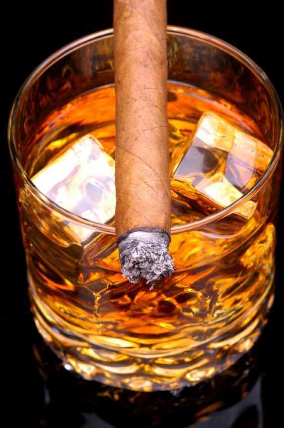 Lit Cigar resting on Glass of Whiskey and Ice cubes - close, vertical