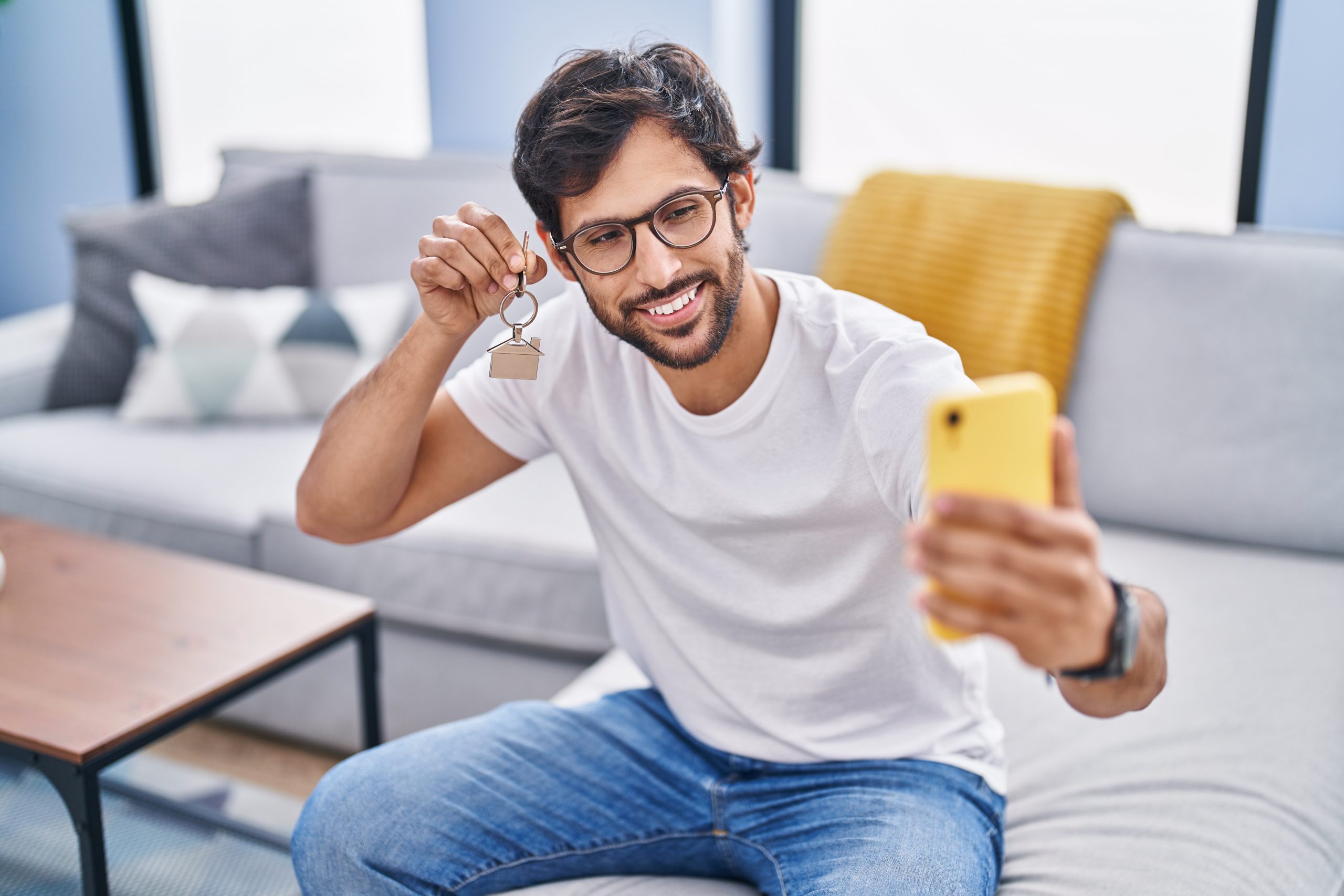 Young hispanic man make selfie by smartphone holding key at home
